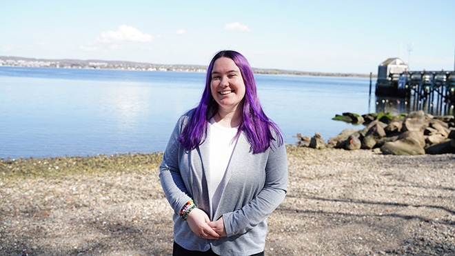 A student standing on the shore of Narragansett Bay with RWU's learning platform in the background