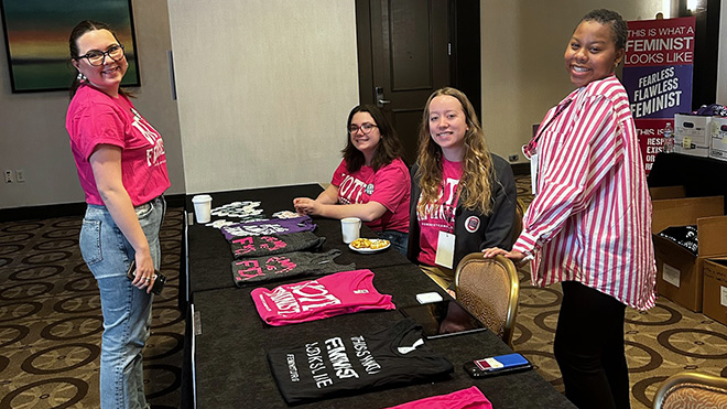 Emma Hall with three of her co-workers at a table selling pink and black feminist t-shirts