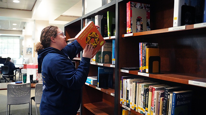 A student places an orange precalculus book onto a shelf in the library