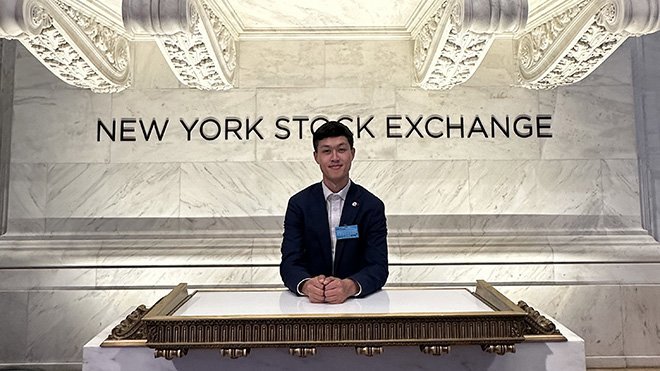 Phillip Call sitting in front of a New York Stock Exchange sign 