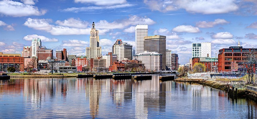 Providence skyline along water showing reflection of buildings under cloudy blue sky