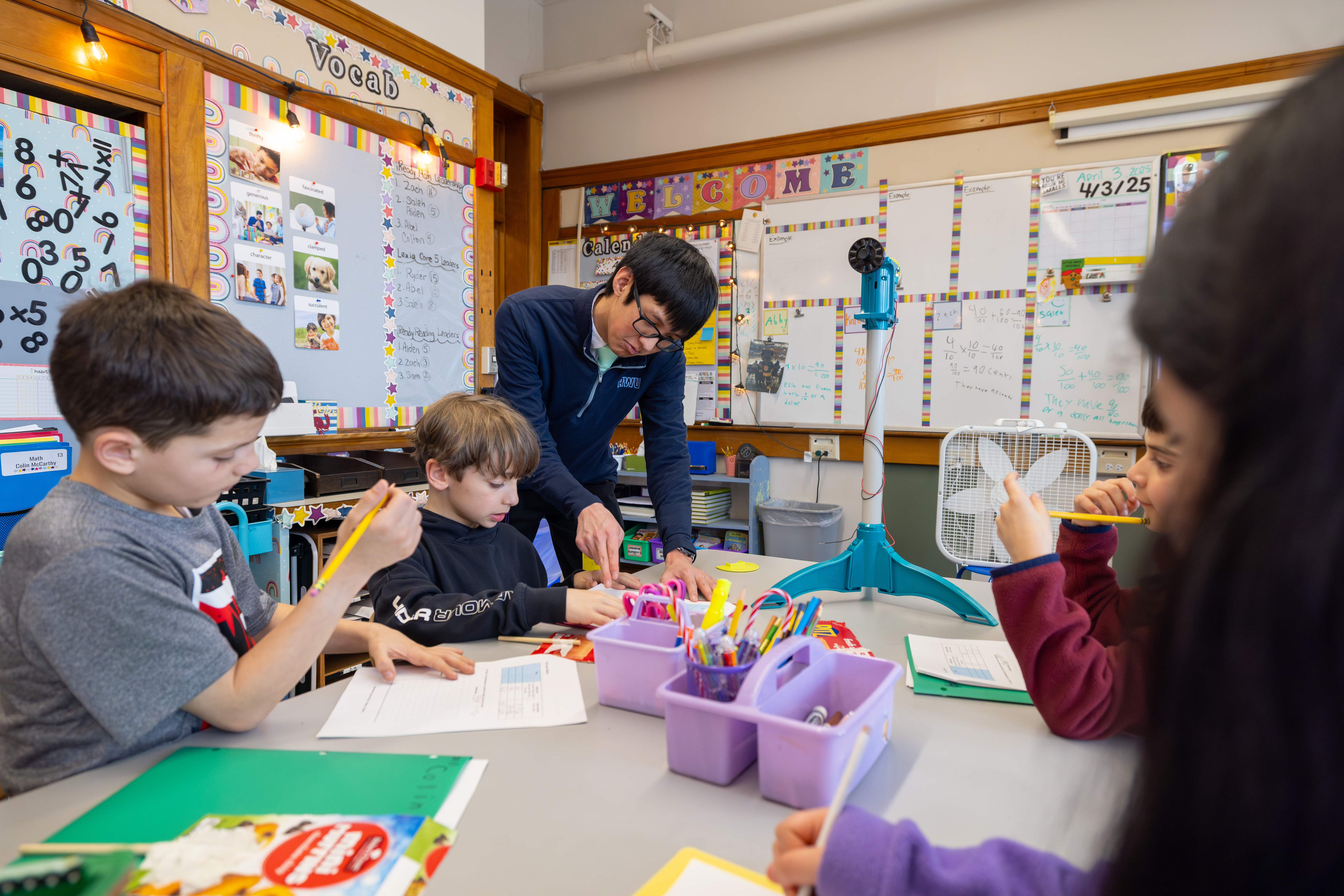 A teacher helps students in a colorful classroom.