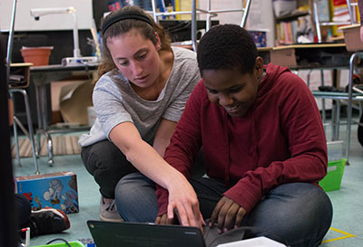 Education student helps a young student with a laptop during a classroom activity.