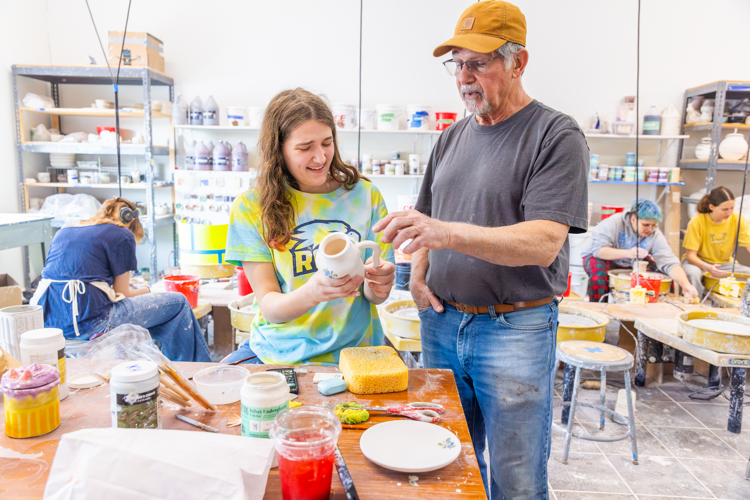 Leonti and a student examine a newly made mug with an ornate handle as he shares feedback, experience, and technical insight.