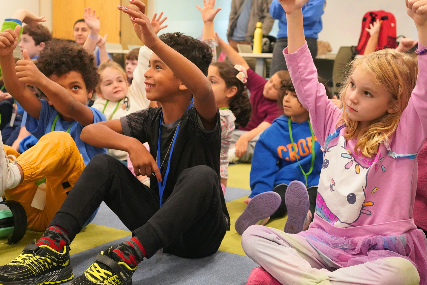 Croft School second graders raise their hands and smile during a group debrief.