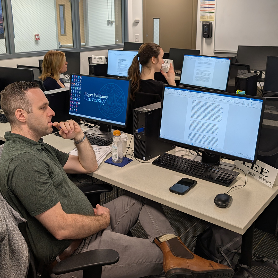 Three people work at computers in a university classroom