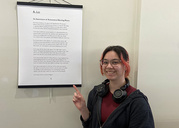 sophomore A. Lee stands next to their poem at Rogers Free Library
