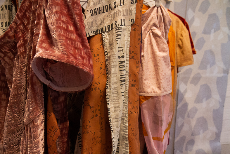 Garments with printed text hanging on rack. 