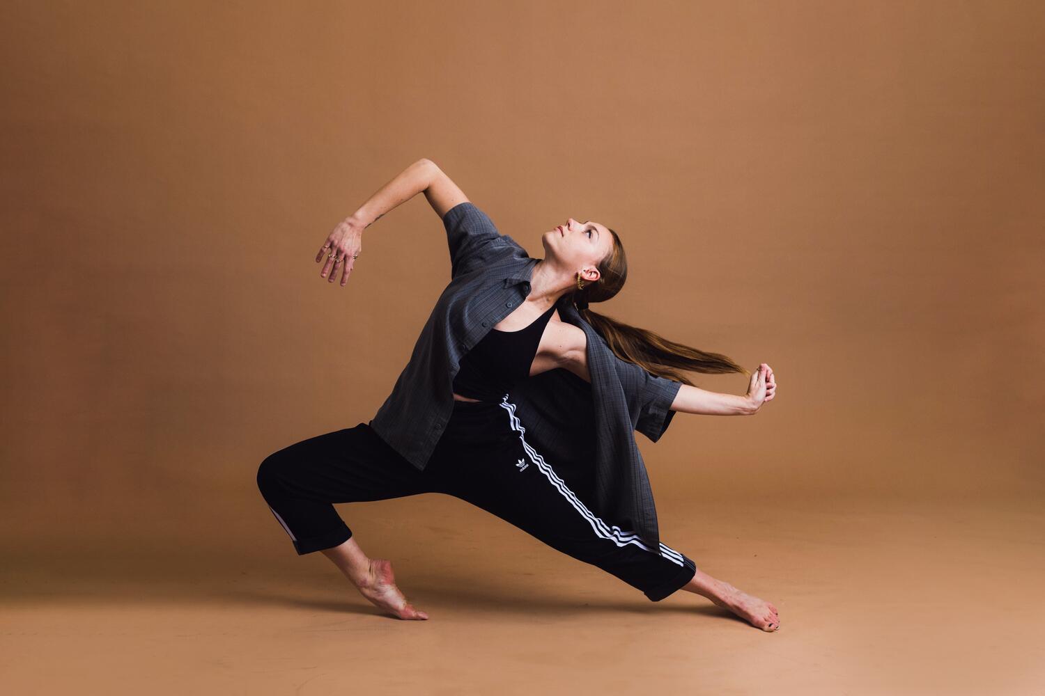 A dancer lunges low with arms extended against a brown background