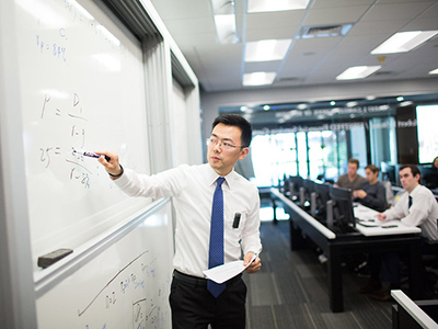 A business professor writing on a whiteboard as students sit in class 