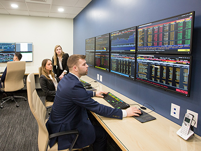Three students looking at stocks on a screen in the trading room 