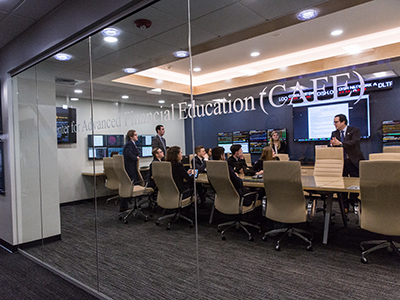 A professor speaking with students sitting around a table inside the trading room