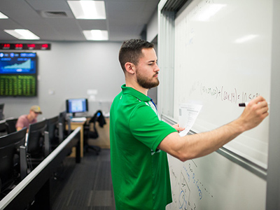 A student wearing a bright green shirt writing on a whiteboard 
