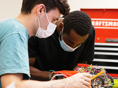 Two Engineering students work on wiring a small model car 