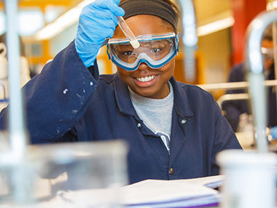 A student wearing safety goggles and holding a dropper in a biology lab
