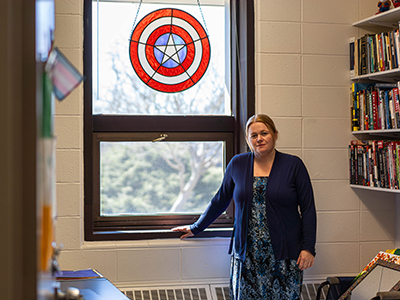 Associate Professor of Political Science Annika Hagley stands in her office under a Captain America stained-glass shield.