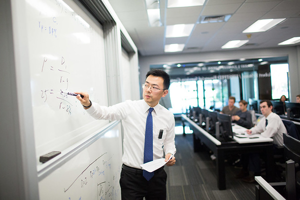 A business professor writing on a whiteboard. 