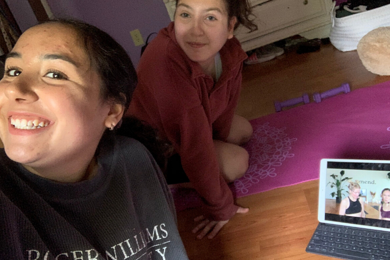 Two people sitting on the floor with a yoga mat and a laptop open to a workout video. 