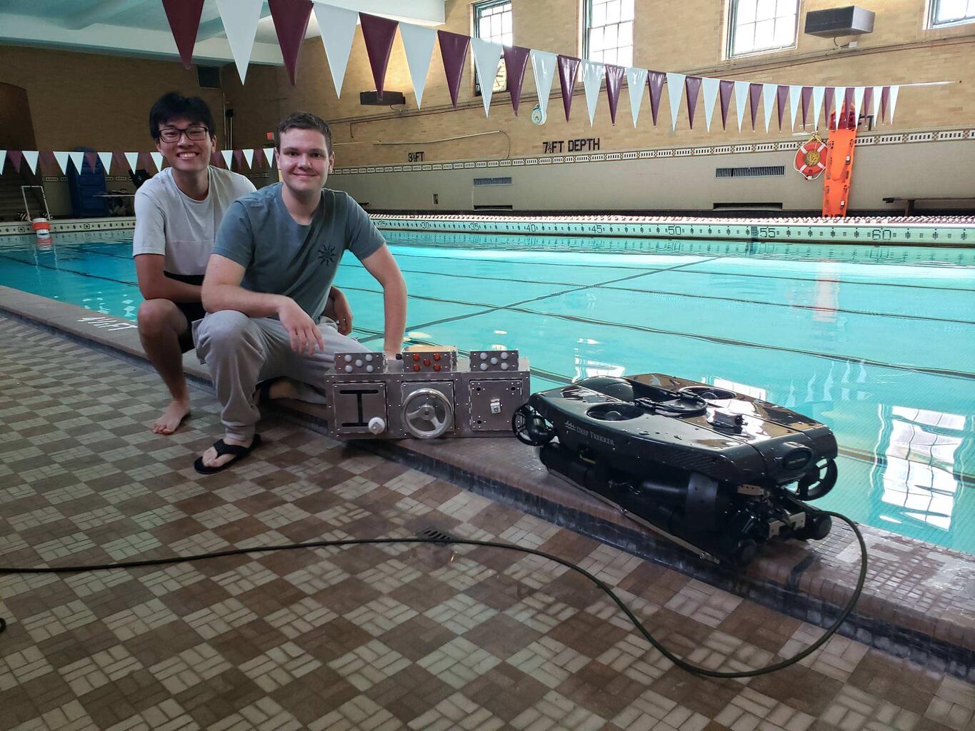 Seniors Chace Kirwan and Louis Zhu stand beside a Deep Trekker underwater robot and the aluminum platform they designed and built for testing in the pool.