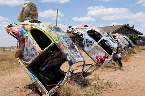 Sculpture: spray painted shells of cars stick up out of the ground