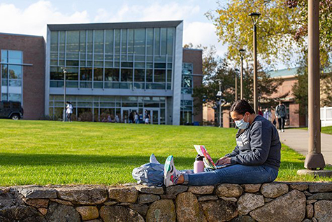 image of student sitting on stone wall in front of Commons on RWU Bristol campus