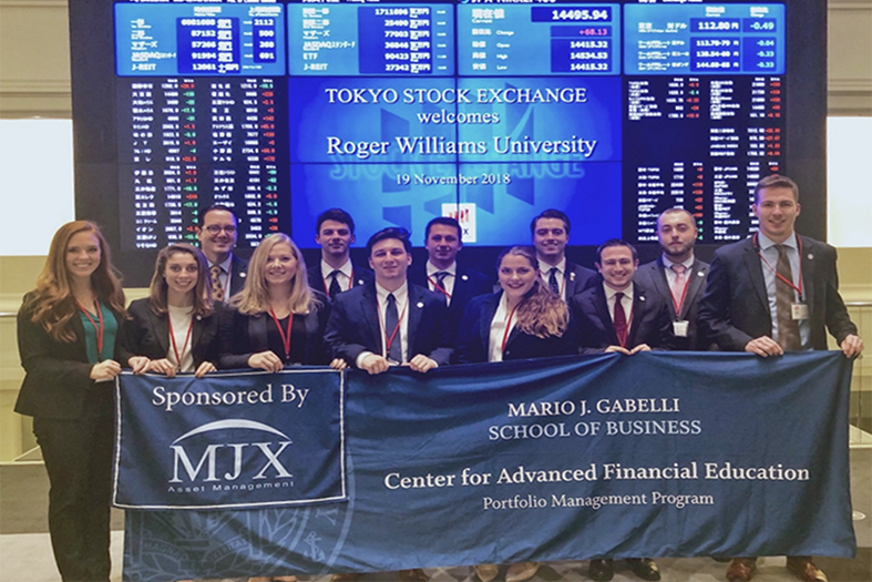 Students stand in front of screens that say Tokyo Stock Exchange Welcomes Roger Williams University Students