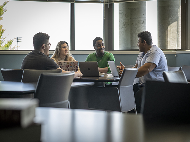 Students sitting at table collaborating with laptops in front of them