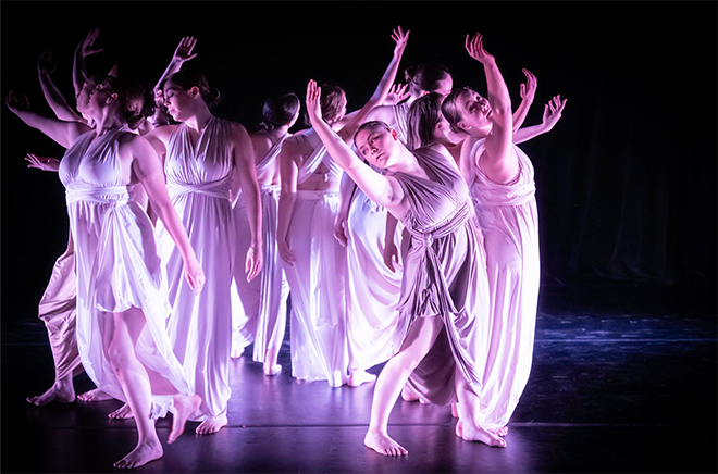 Dancers wearing white toga style dresses lit up in pink light - "Light Circle"