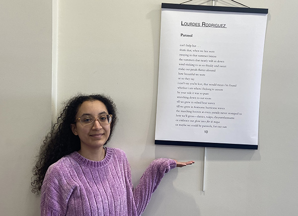 Sophomore Lourdes Rodriguez stands in the Rogers Free Library next to her poem "Parasol" which is displayed on the wall