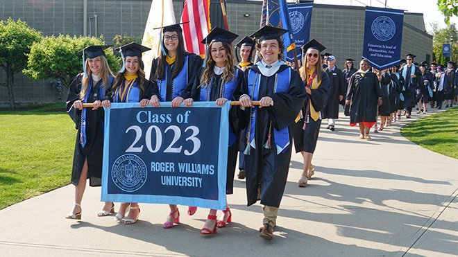 Graduates carry the Class of 2023 banner.