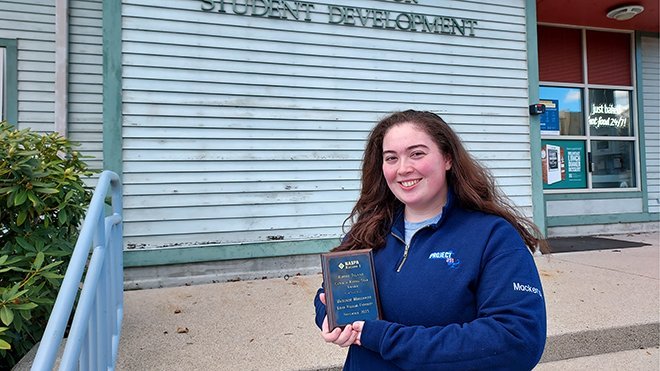 Mackenzie Morgenweck holds her NASPA award outside the Student Development building