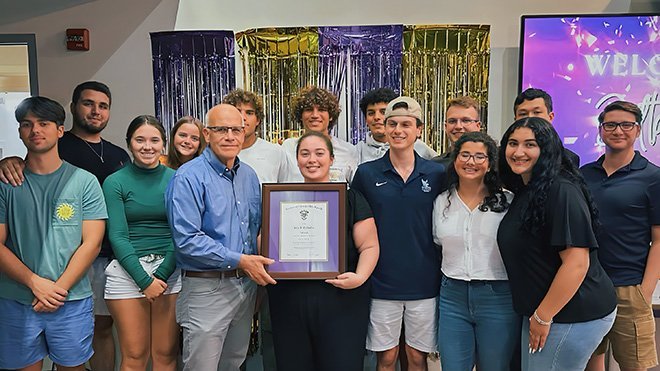 Professor John McQuilkin holding his award surrounded by students in Delta Sigma Pi