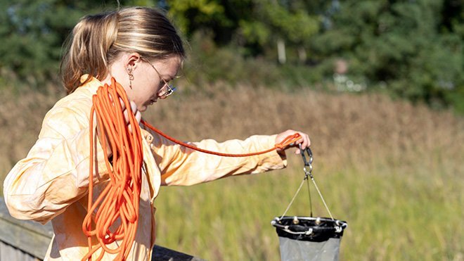 Michelle Kryl, wearing an orange lab coat, pulls a net out of the water.