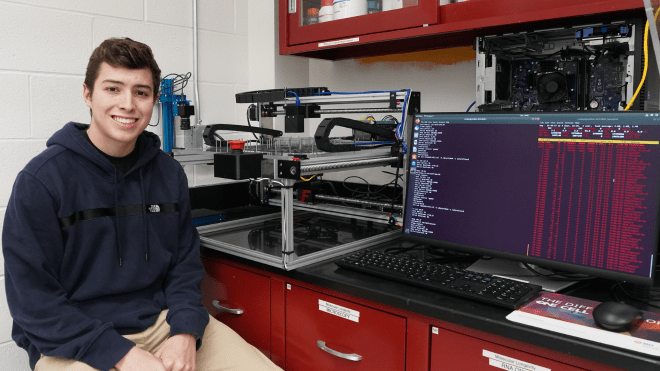Colton Pelletier proudly sits next to his robotic creation in the lab. 
