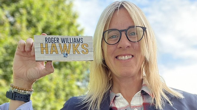 A photo of Kelly Scafariello holding a Roger Williams Hawks sign