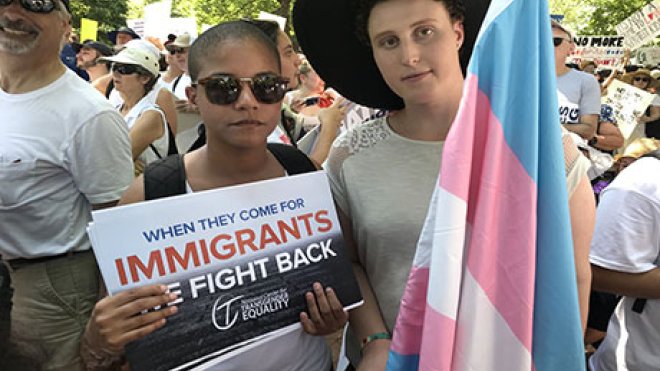 Two people standing with a flag and a sign.
