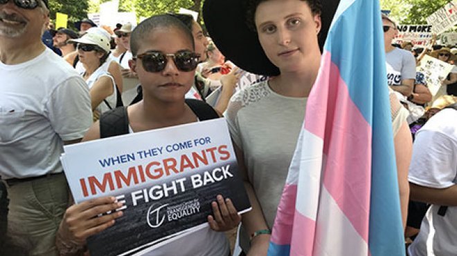 Two people standing with a flag and a sign.