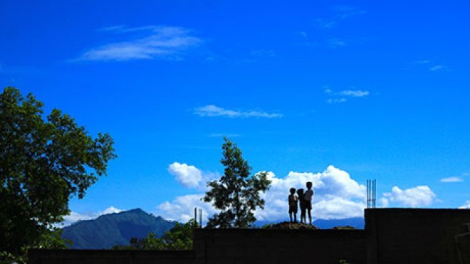 Three children are standing on the roof of a building in the Dominican Republic.