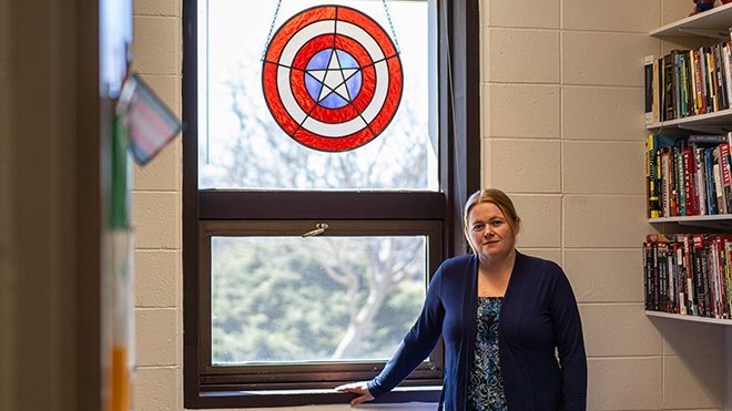 image of RWU Professor Annika Hagley standing under the Captain America stained glass shield hanging in her office window