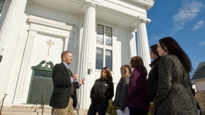 Professor lectures students on the steps of a historic building.