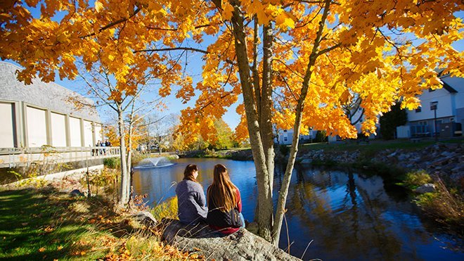 Two students sitting outside on campus in the fall. 