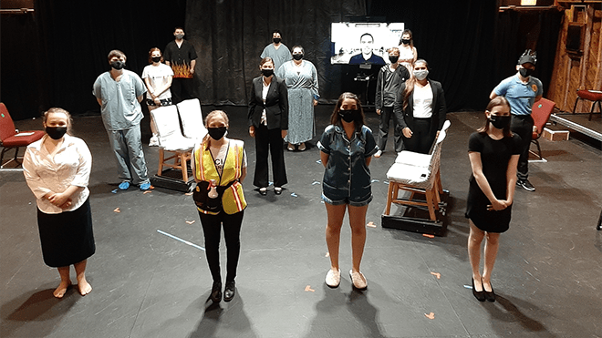 Students stand on a stage, wearing masks and six feet apart