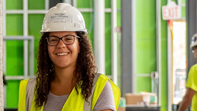 A female student smiles wearing an RWU construction hat and safety vest