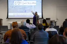 Presenter, Dr. Jennifer Pearce, pointing to image on projector screen in front of audience.