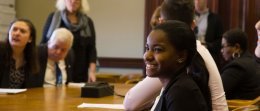 A student is smiling as she listens to a discussion between students, faculty and local elected officials