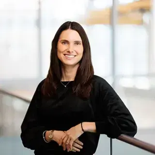 Headshot of Lillian Jeznach, woman with brown hair and a black top leaning against a railing.