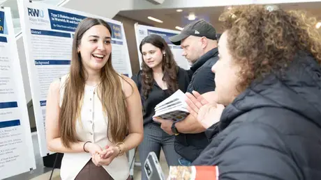 An undergraduate student presents their research in the GHH atrium.