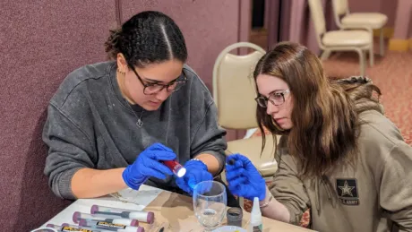 Two RWU students using a blacklight to find fingerprints on a glass cup.