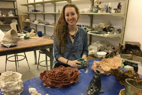 Student seated in the ceramics studio, surrounded by her art.