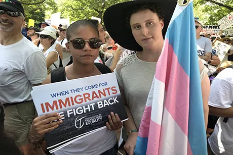 Two people standing with a flag and a sign.